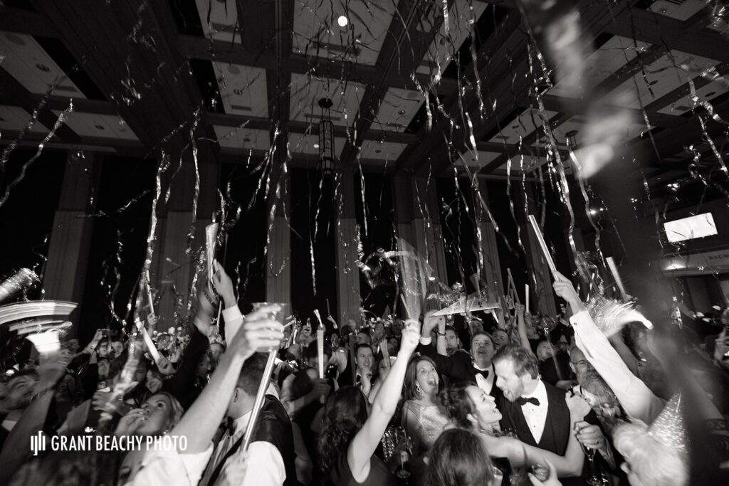 A black and white photo of wedding guests Danceing the night way, slight blur of hands in the air as streamers cascade over them