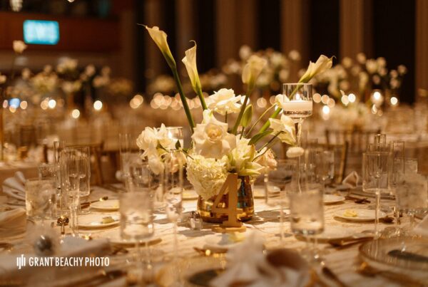 Spotlighted Wedding Tablescape with a White floral centerpiece including Calla Lillies, Roses, and hydrangeas in a Gold Container